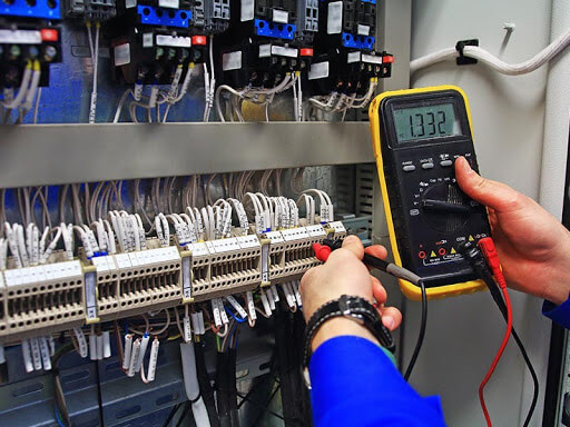 Engenheiro verificando um equipamento com a utilização de um voltímetro.